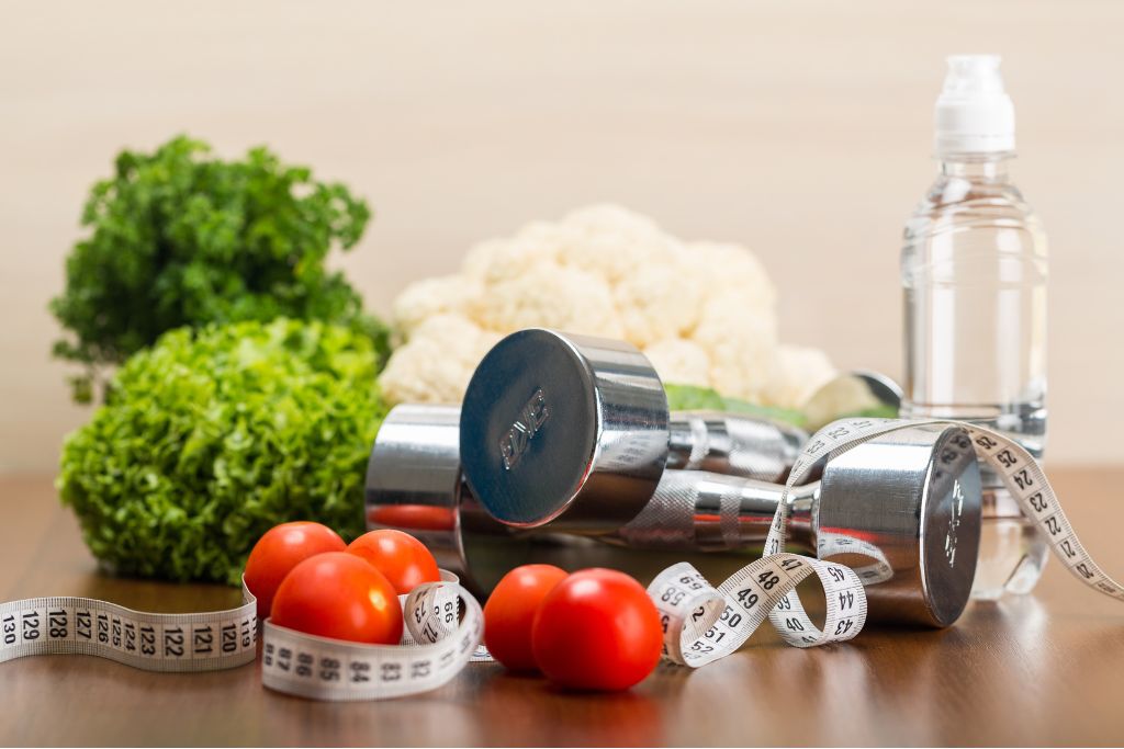 Whole foods, dumbbells, and a measuring tape symbolizing how macronutrients work for fat loss and muscle gain.