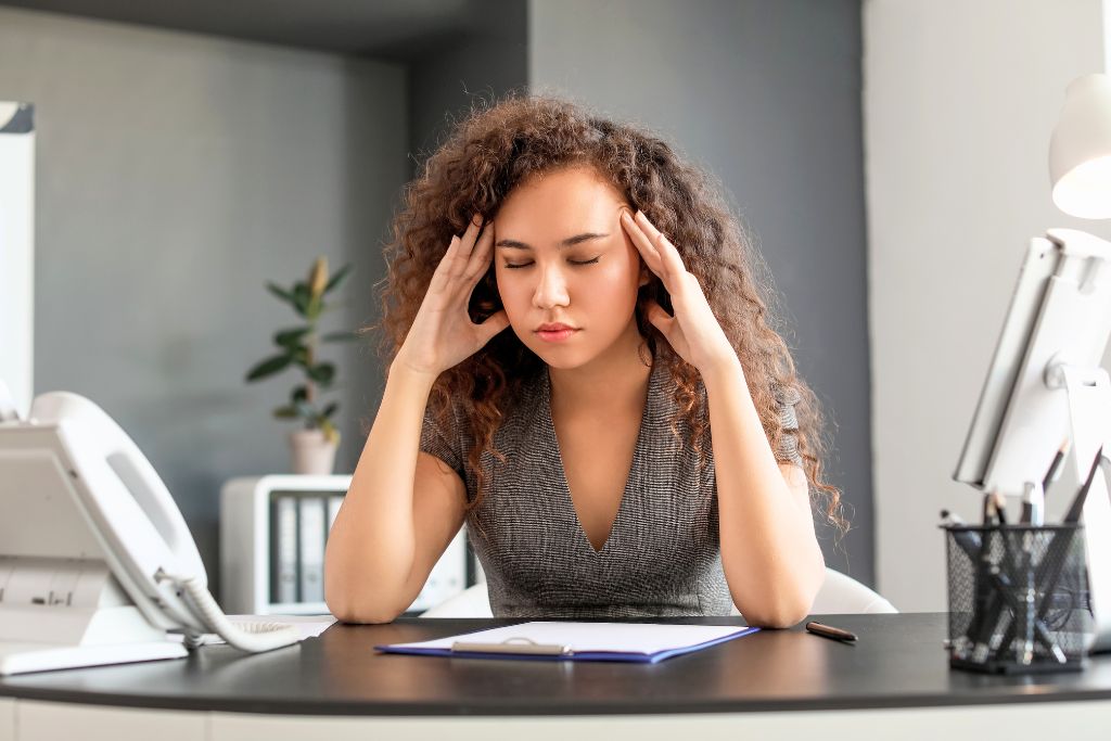 Can burnout cause anxiety? Woman at desk with stress and tension headaches