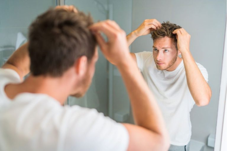 Man checking hairline in bathroom mirror, concerned about thinning hair and wondering if hair loss from stress can grow back.