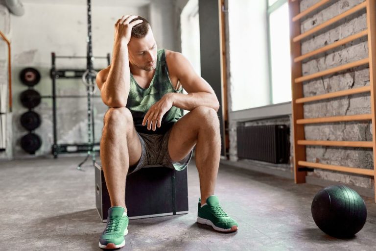 Athlete sitting in a gym looking stressed after training, representing hair loss in athletes caused by stress, overtraining, and nutrient depletion.