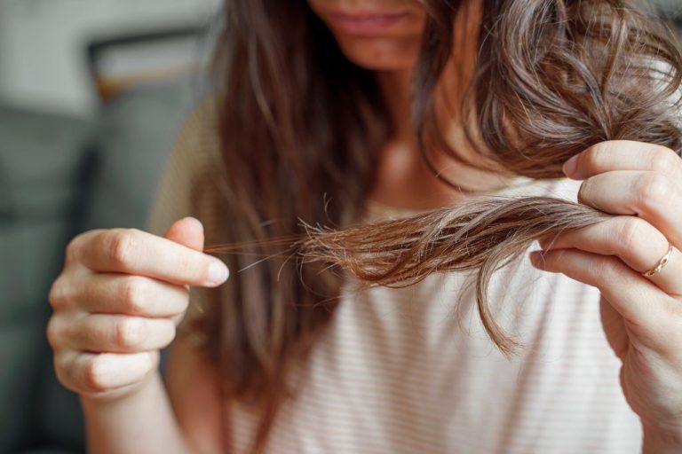 Woman examining strands of her hair for breakage and thinning, showing signs of patchy hair loss after COVID recovery.