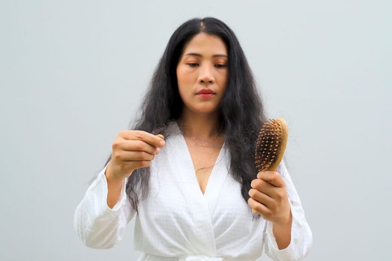 A woman looking at strands of hair shed onto her brush, illustrating excessive hair loss commonly seen in telogen effluvium compared to androgenetic alopecia.